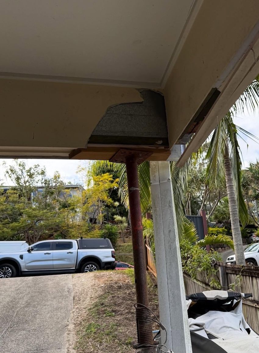 A damaged corner of an outdoor roof eave reveals the wooden framework and roof shingles, supported by a metal post — RAC Carpentry Services in Pimpama, QLD