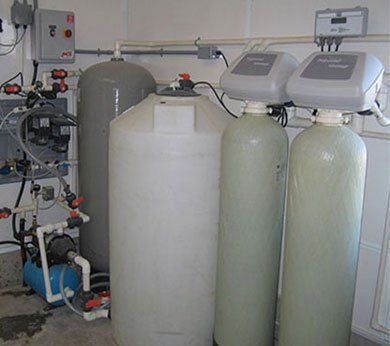 Équipements de traitement des eaux industrielles avec de grands réservoirs blancs et verts, des tuyaux et des unités de contrôle dans une salle technique