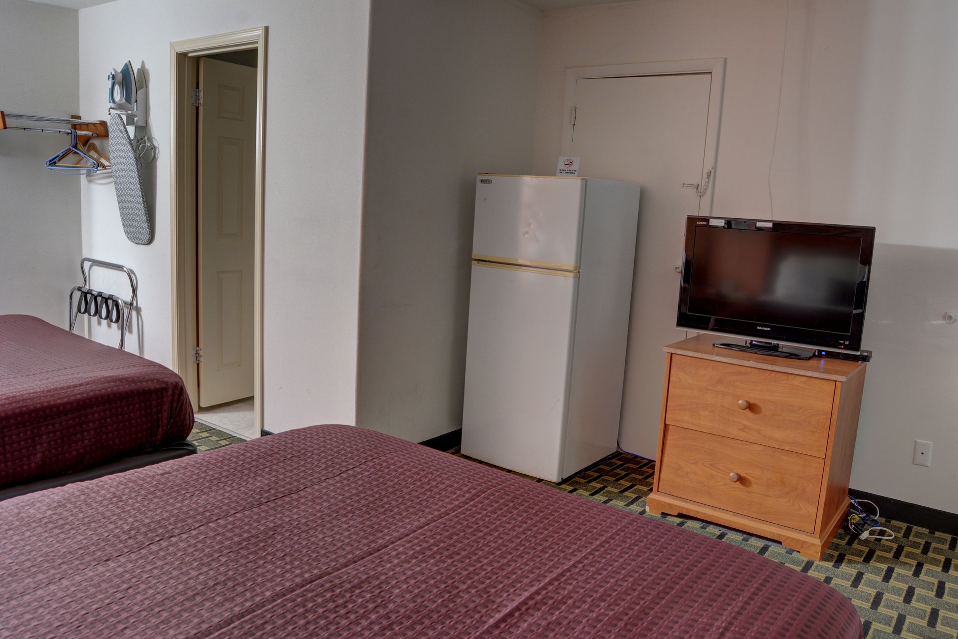 Hotel room with two beds, refrigerator, dresser with TV, and open doorway to a bathroom.