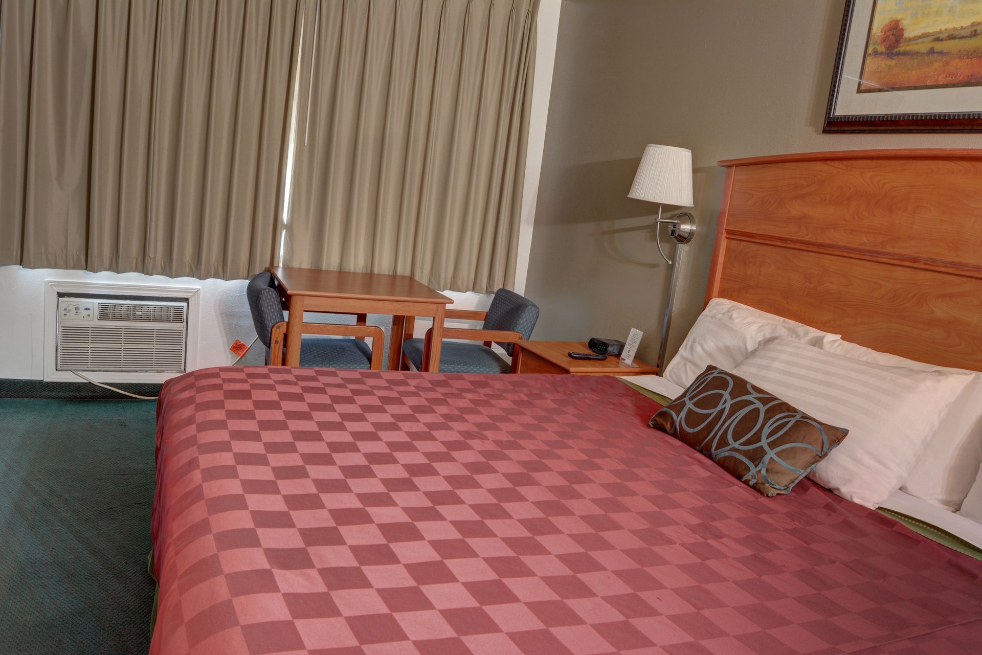 A hotel room with a bed covered in a checkered maroon comforter. 