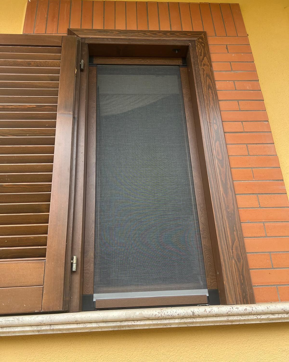 Una finestra con persiane di legno e una zanzariera
