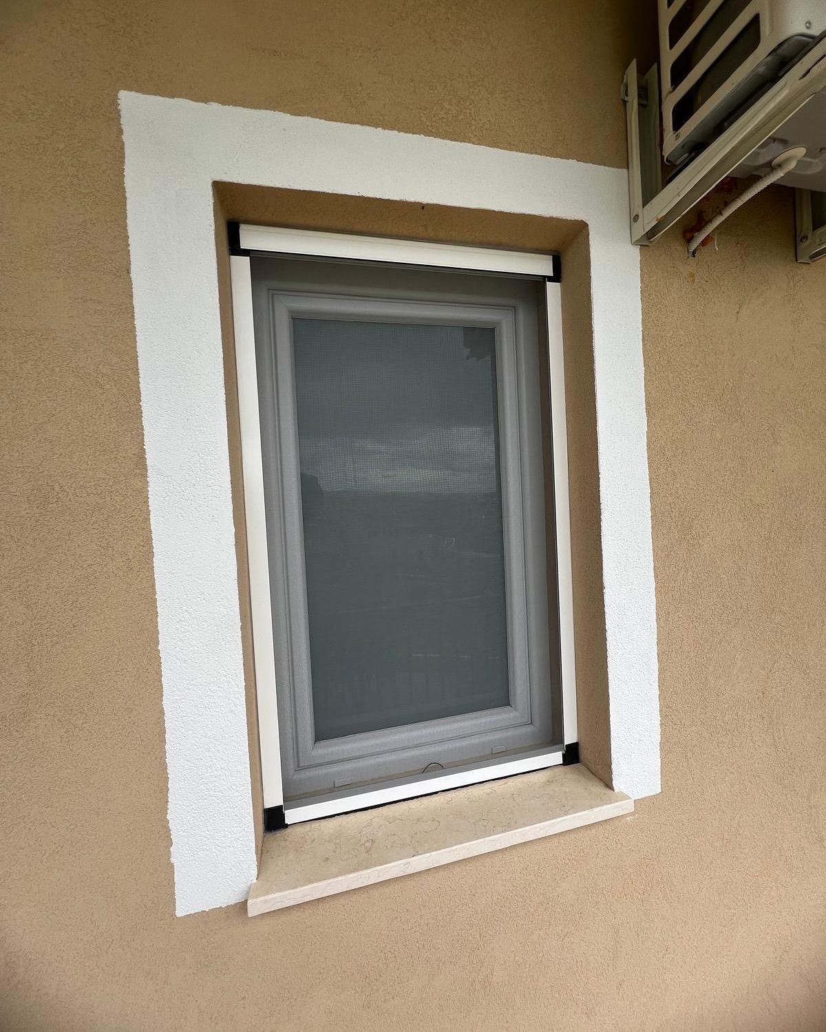 Una finestra con una zanzariera si trova sul lato di un edificio.