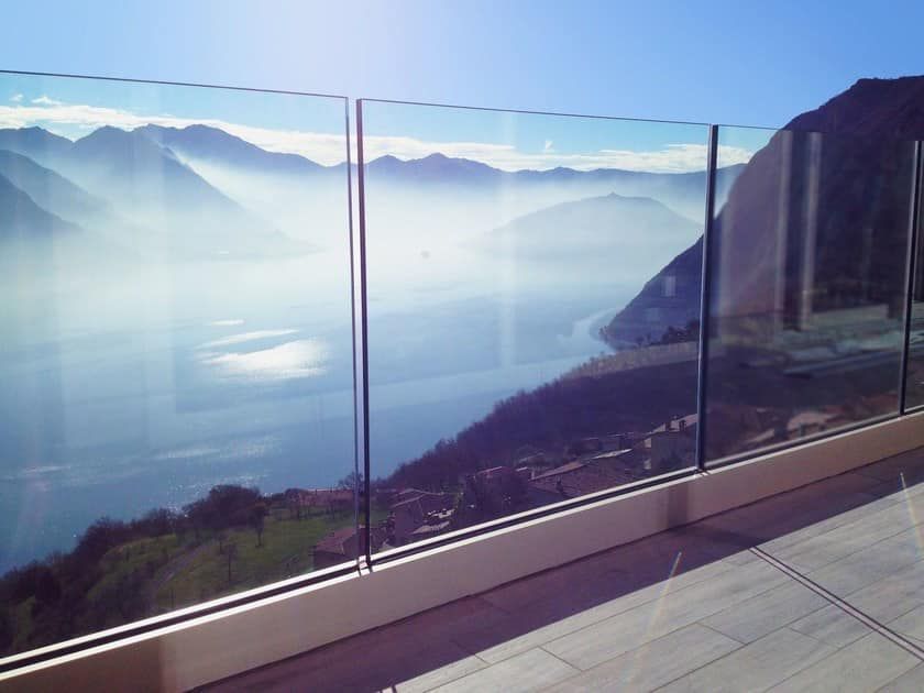 Un balcone con ringhiera in vetro con vista sul lago e sulle montagne.