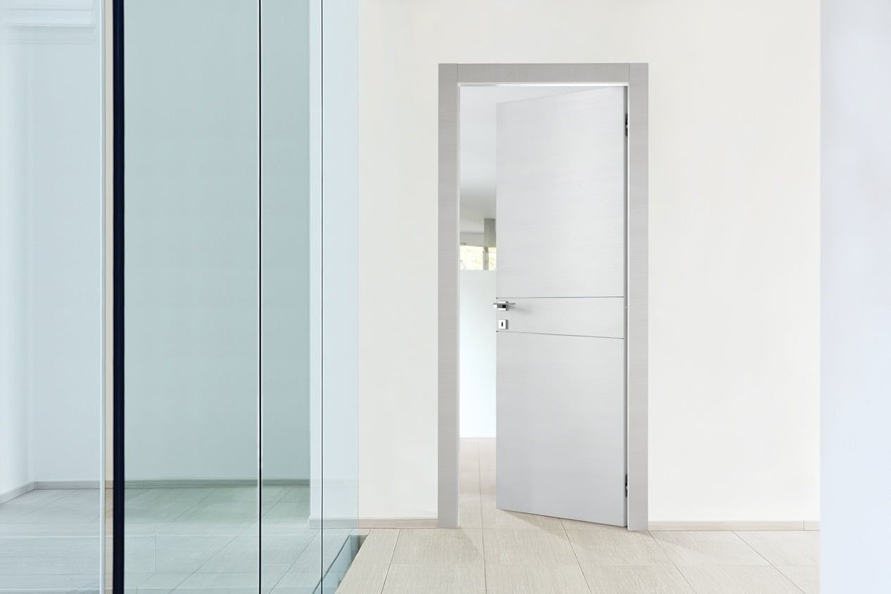 Corridoio minimalista con parete in vetro e porta bianca aperta in una stanza luminosa