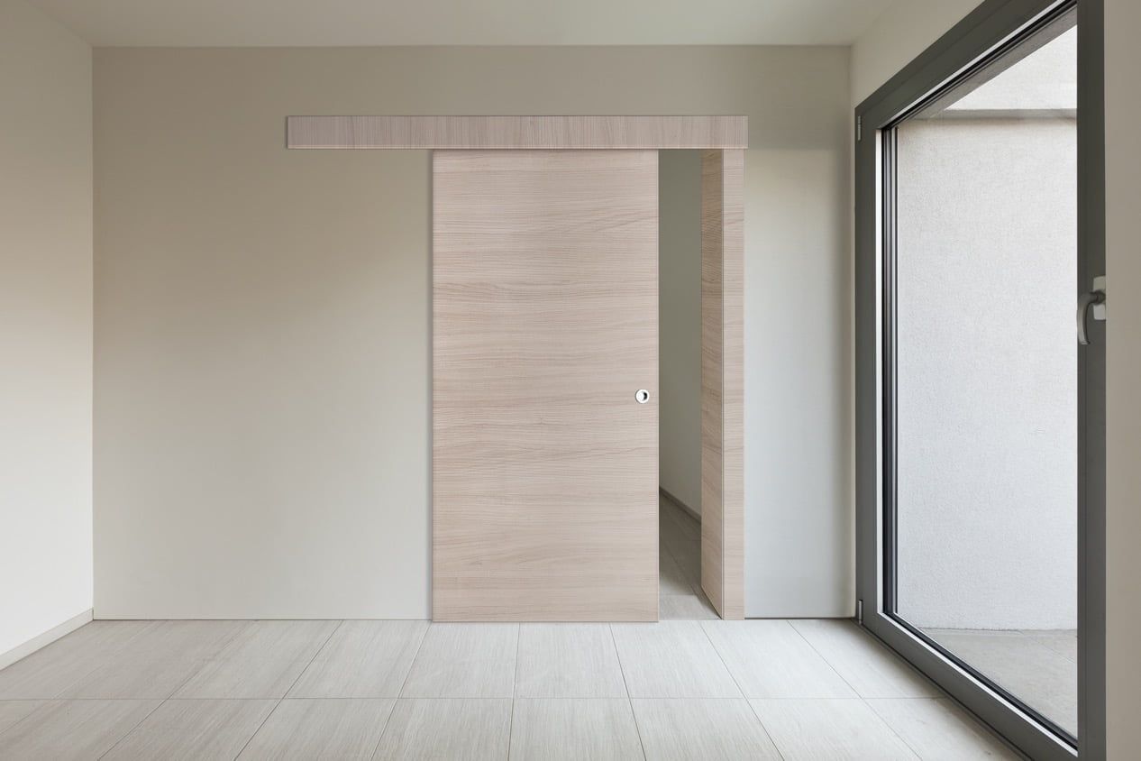 Stanza minimalista vuota con porta scorrevole in legno chiaro e grande finestra in vetro sulla destra.