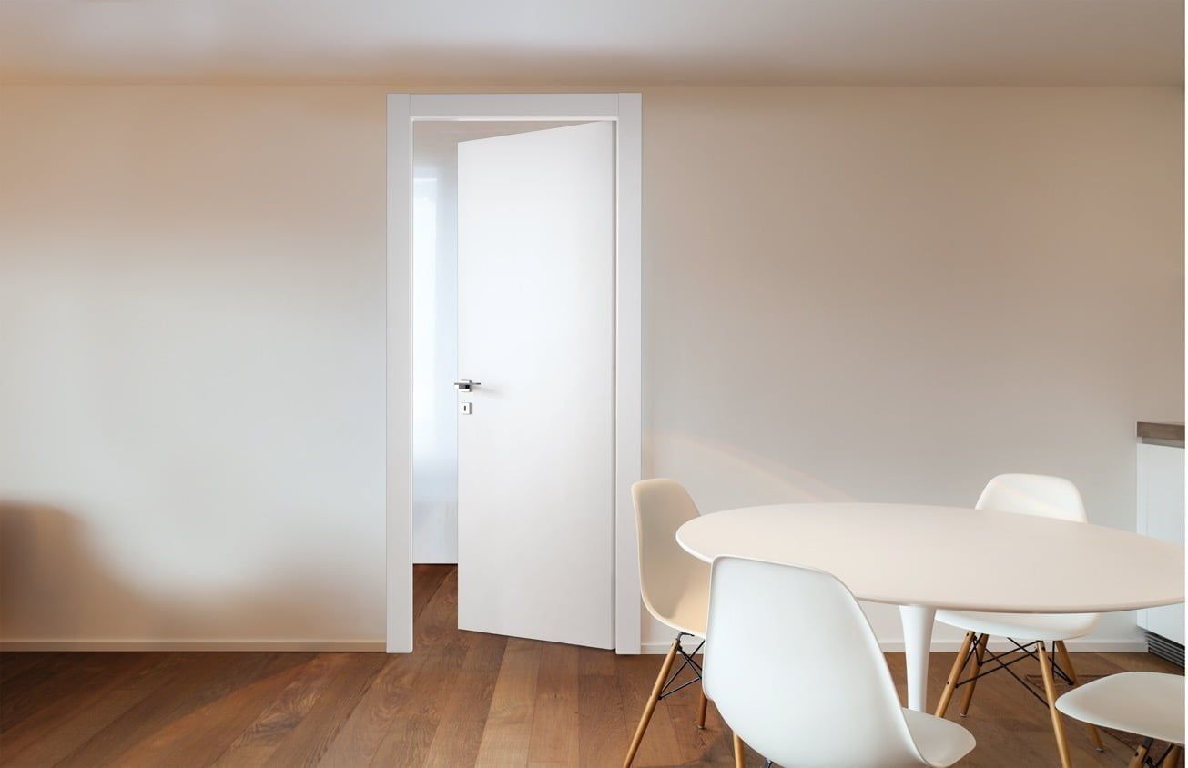 Sala da pranzo minimalista con tavolo e sedie bianchi, pavimento in legno e porta aperta su pareti beige.
