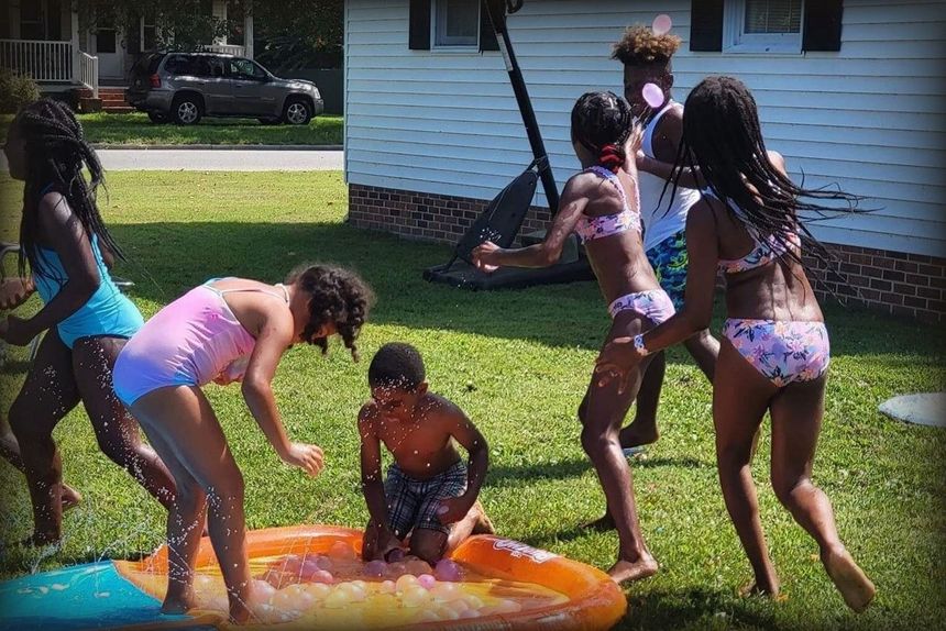 Children playing in a small pool, splashing water on a sunny lawn.