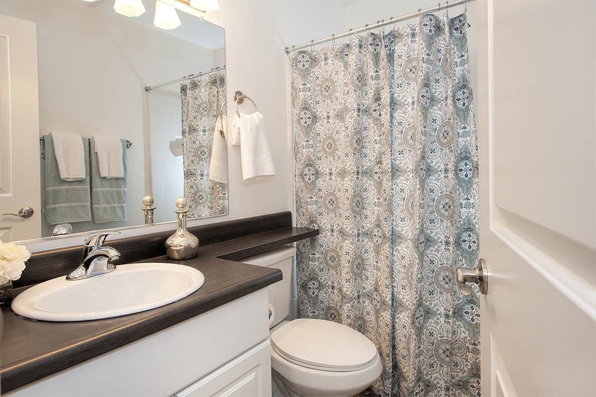 Bathroom with white sink, mirror, toilet, and a blue patterned shower curtain at Marina's Edge.