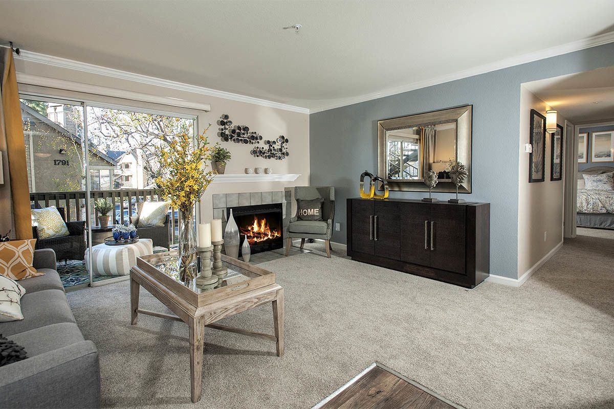 Living room in an apartment with a fireplace, grey sofa, and sliding glass door to the balcony at Marina's Edge.