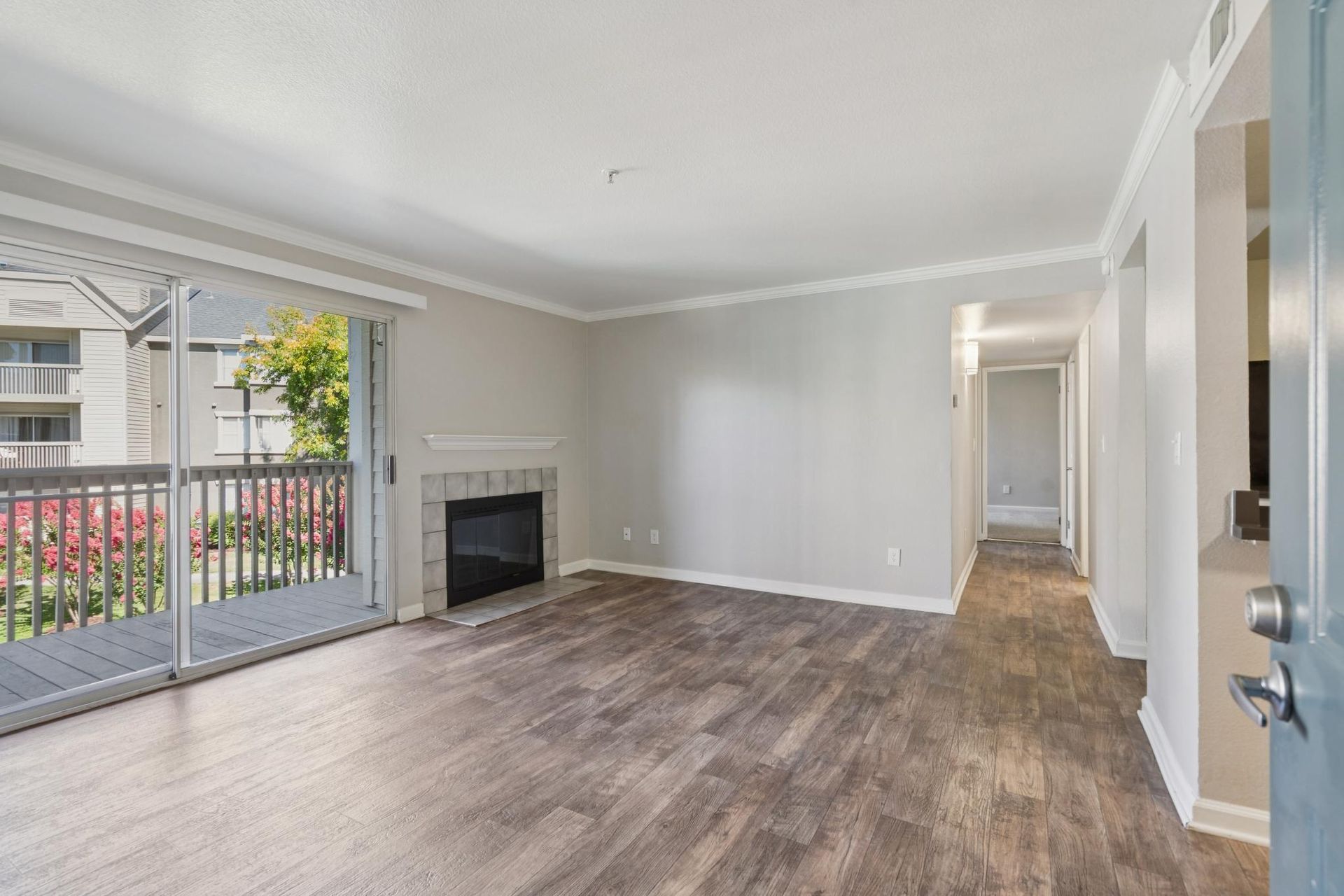 Empty living room with gray walls, wood floors, fireplace, and sliding glass doors to a balcony.