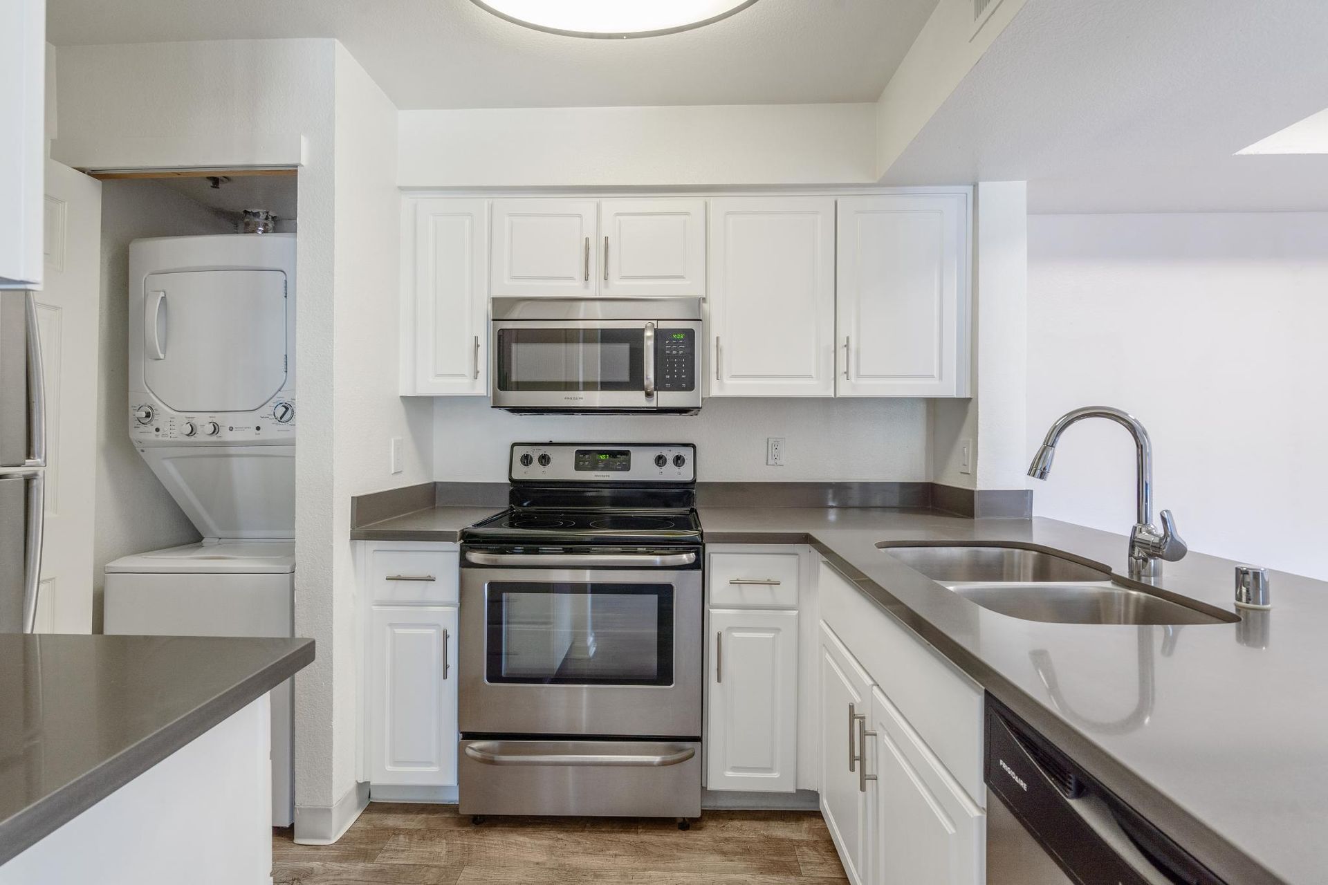 Modern white kitchen with stainless steel appliances, gray countertops, and stacked washer-dryer nook