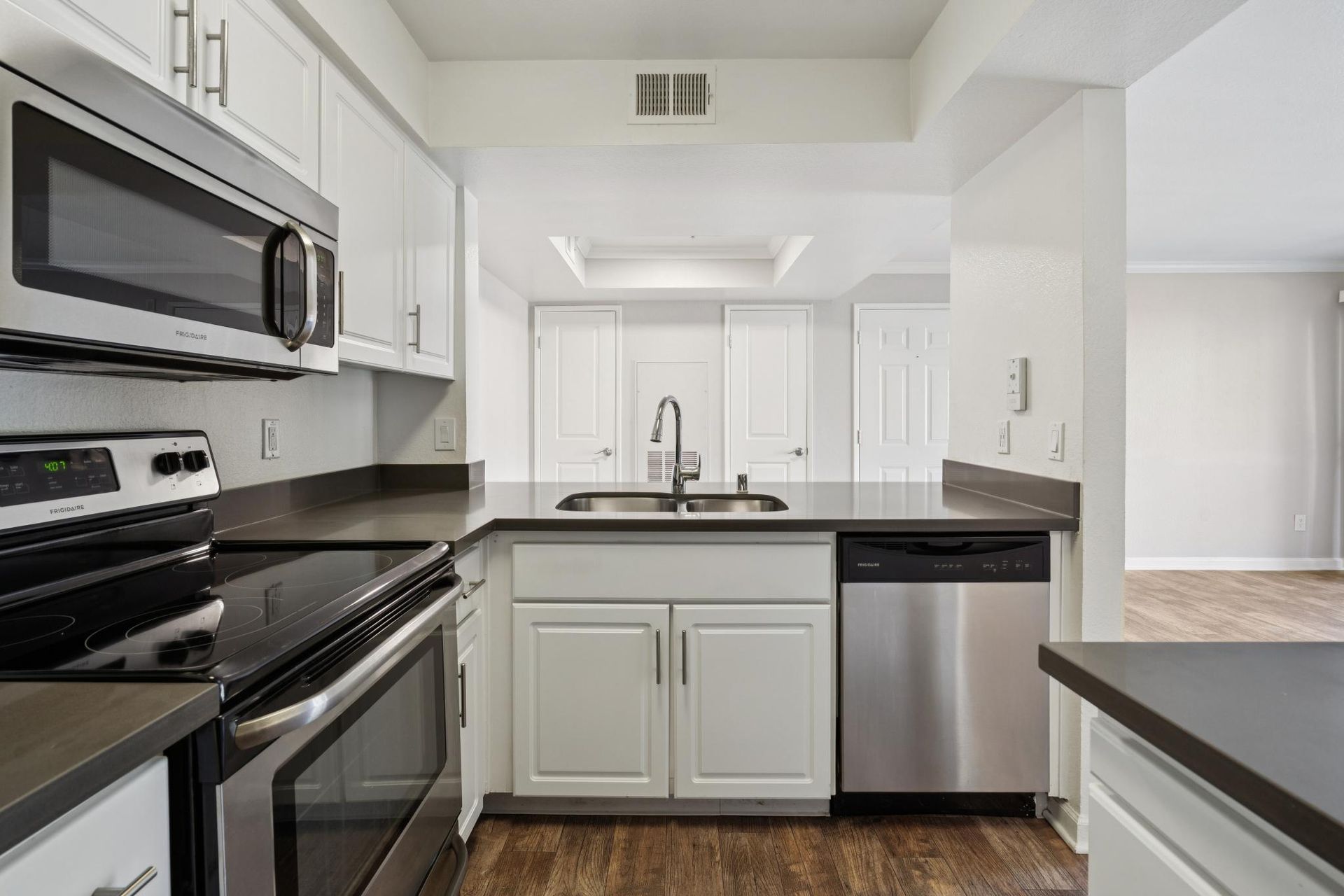 Modern white kitchen with stainless steel appliances, black countertops, and a central sink island