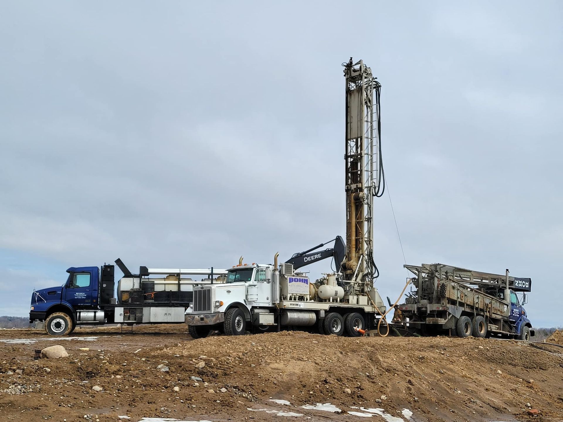 A truck and a drilling rig are sitting on top of a dirt field.