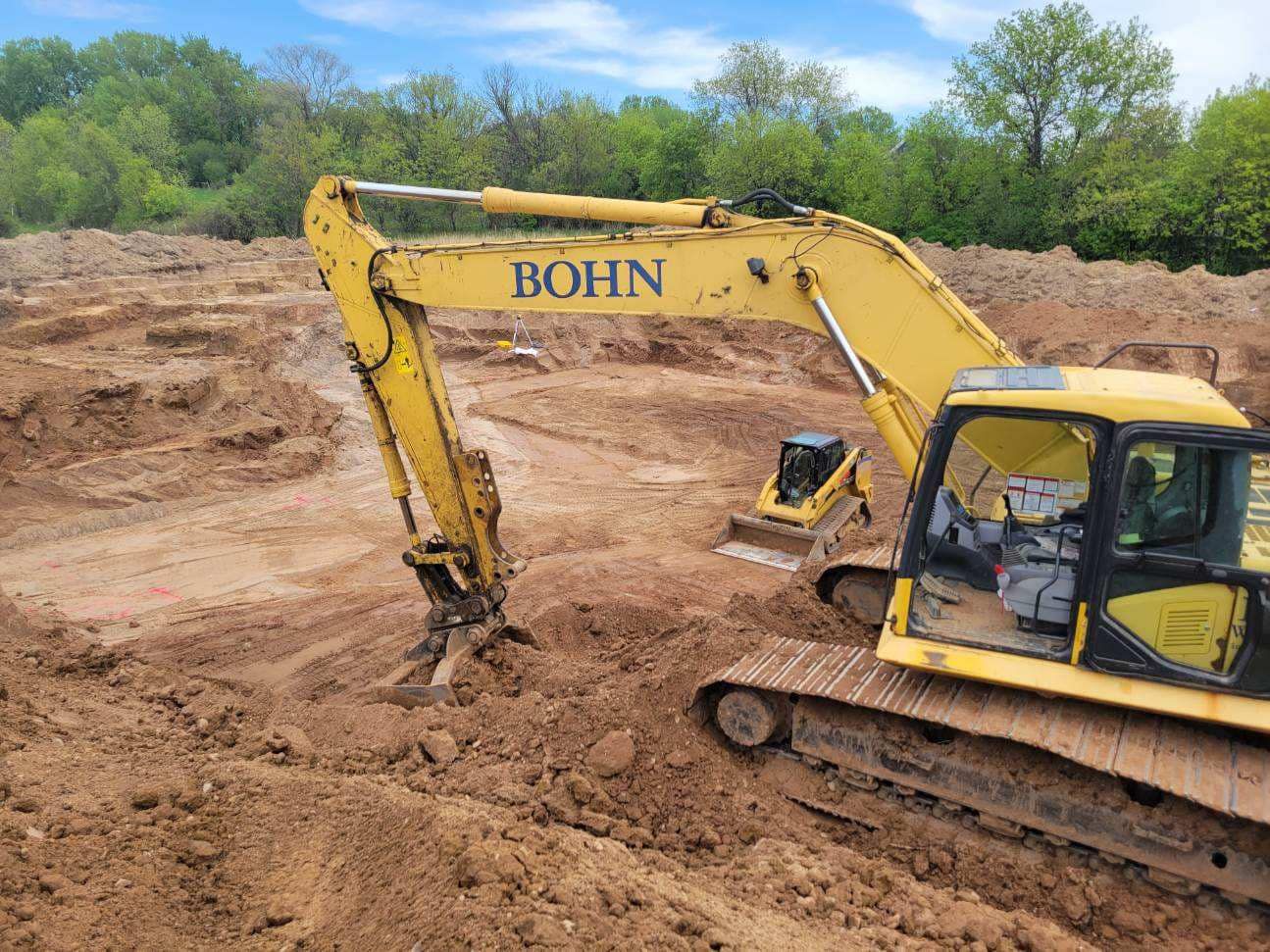 A yellow excavator is sitting in the middle of a dirt field.