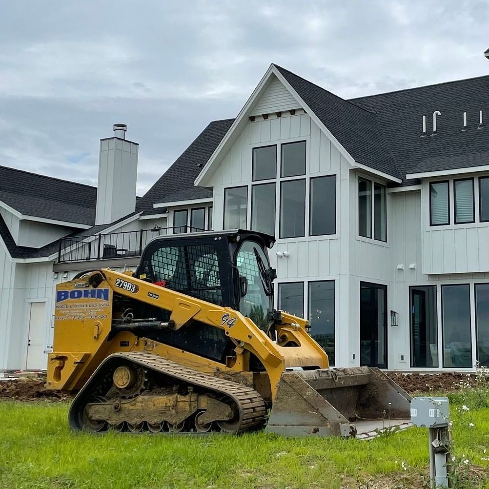 A yellow bulldozer is parked in front of a large white house