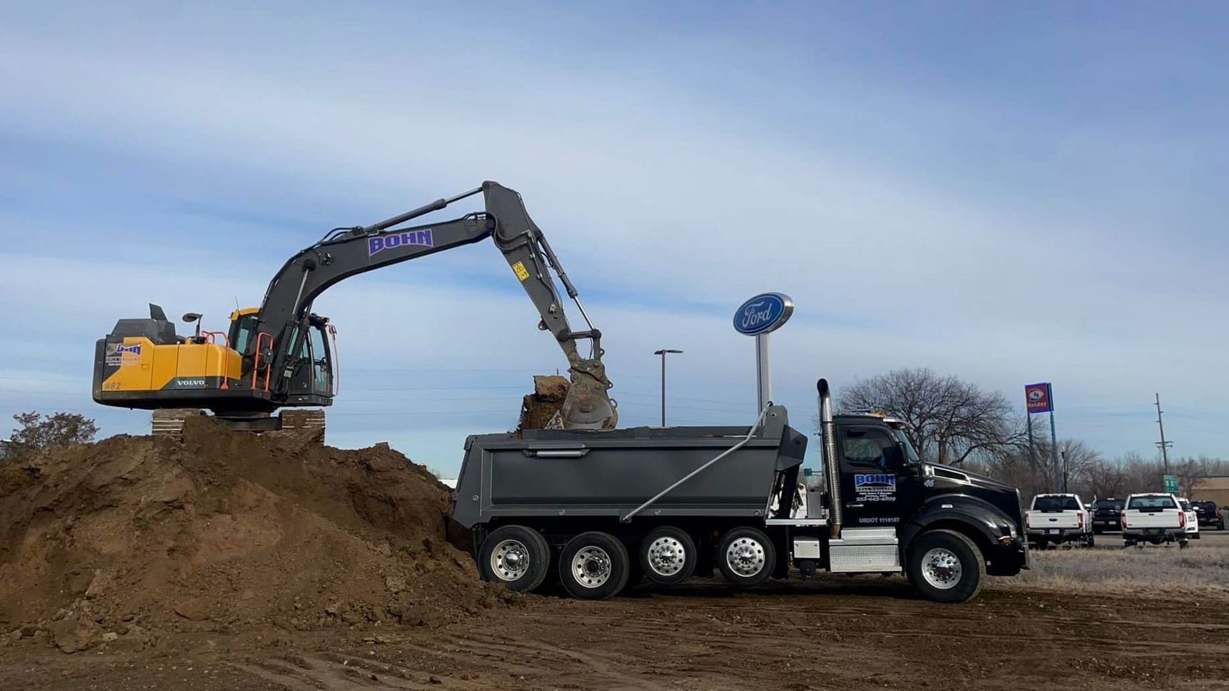 A dump truck is being loaded with dirt by an excavator.