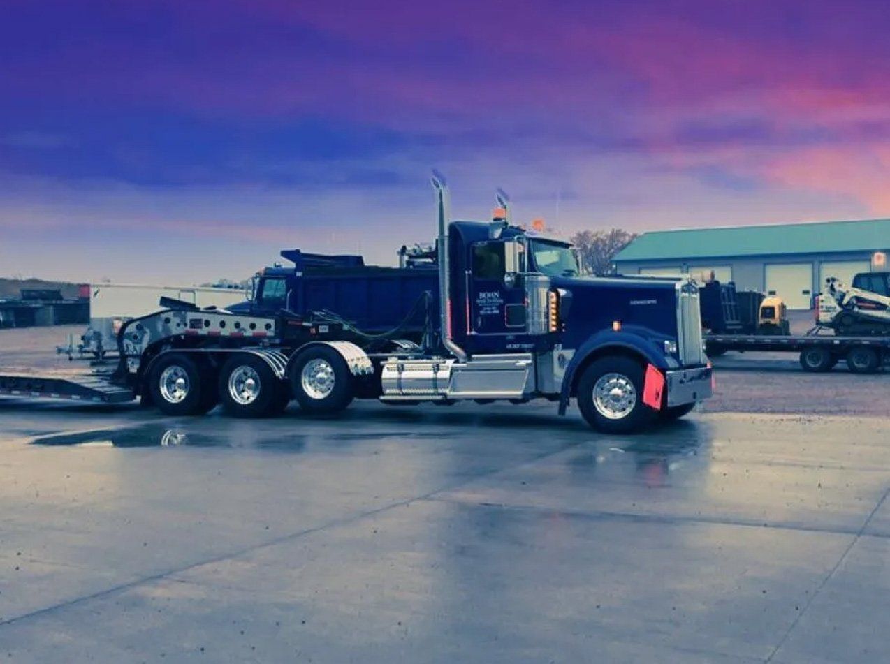 A blue semi truck is parked in a parking lot with a trailer attached to it.