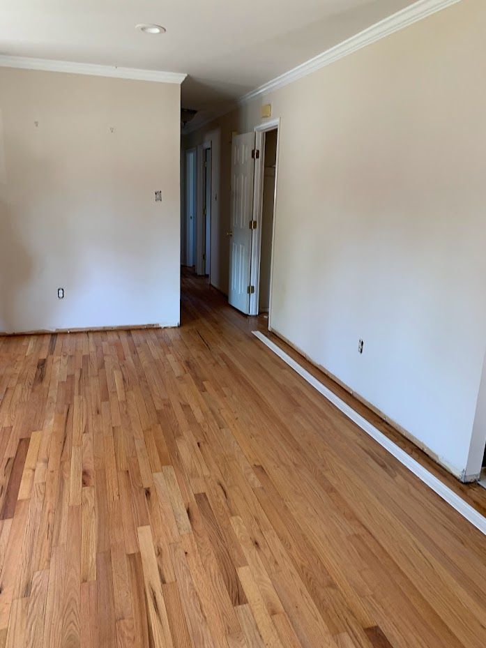 An empty living room with hardwood floors and white walls.