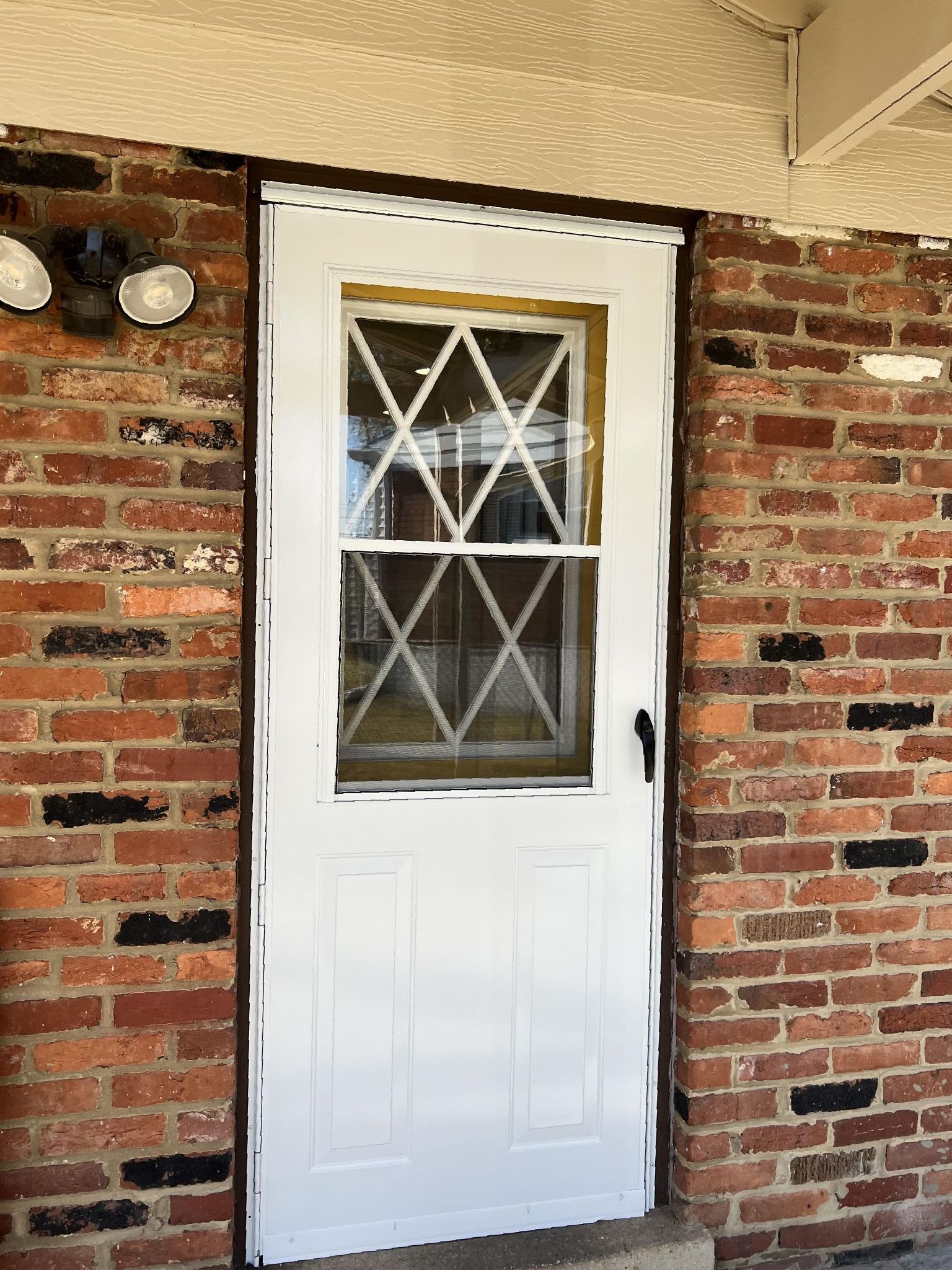 A white door with a window on a brick wall.