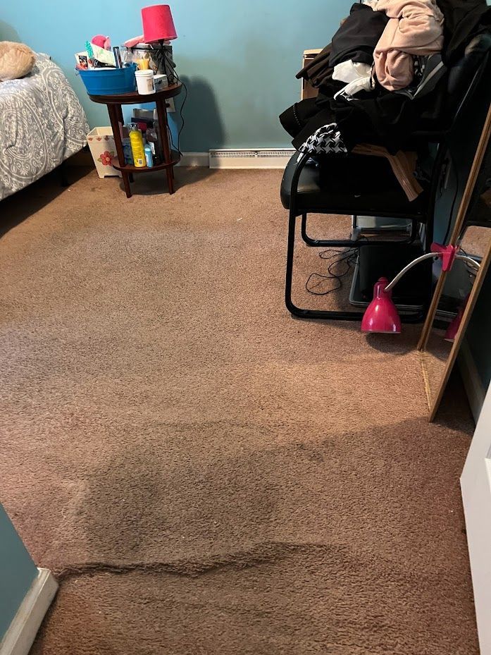 A bedroom with a carpeted floor , a chair , a table and a mirror.