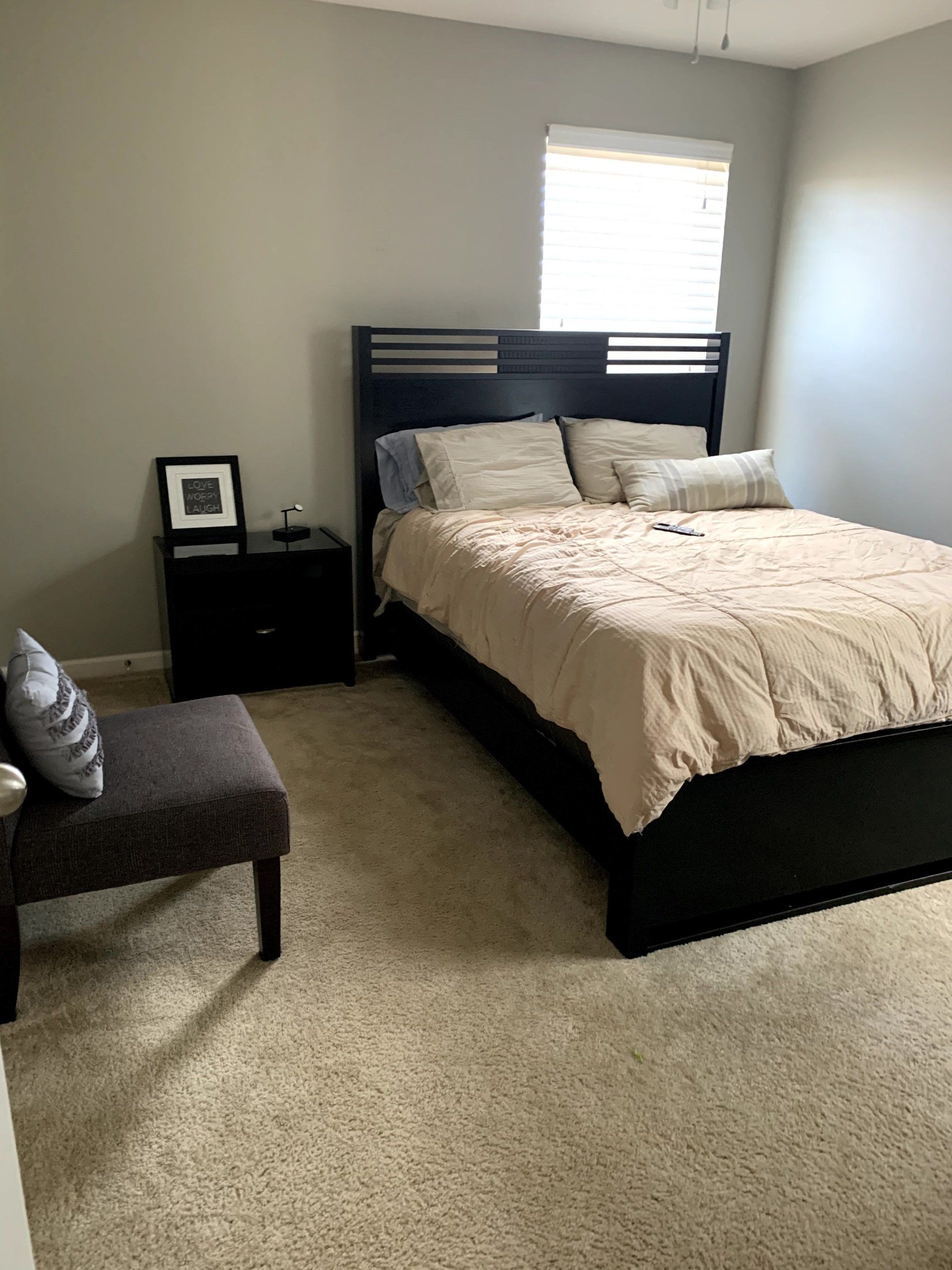 A bedroom with a bed , nightstand , chair and window.