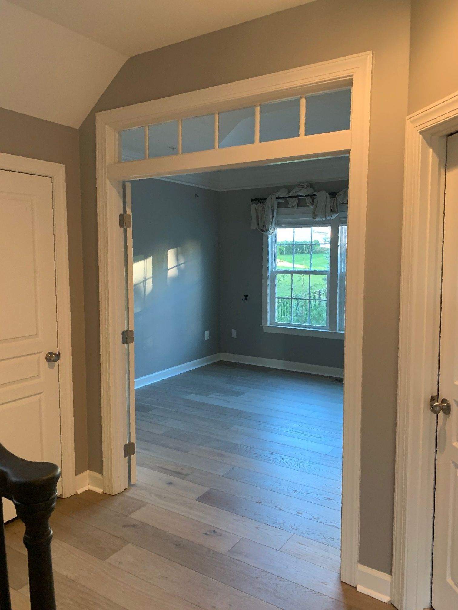 A hallway leading to a living room with hardwood floors and a window.