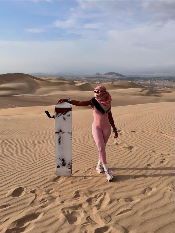 Woman jumping in the air against a bright blue sky, over a sandy desert landscape.