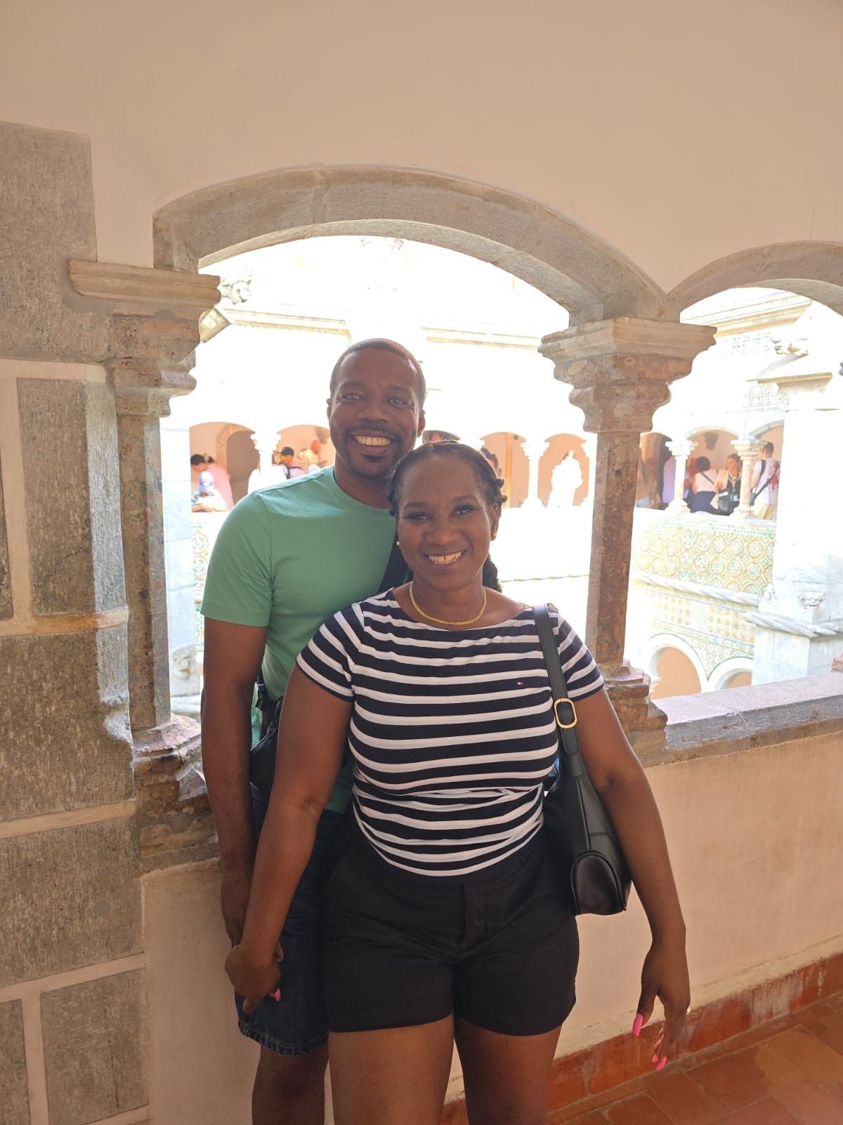 A smiling couple poses for a photo in a stone-arched balcony corridor.