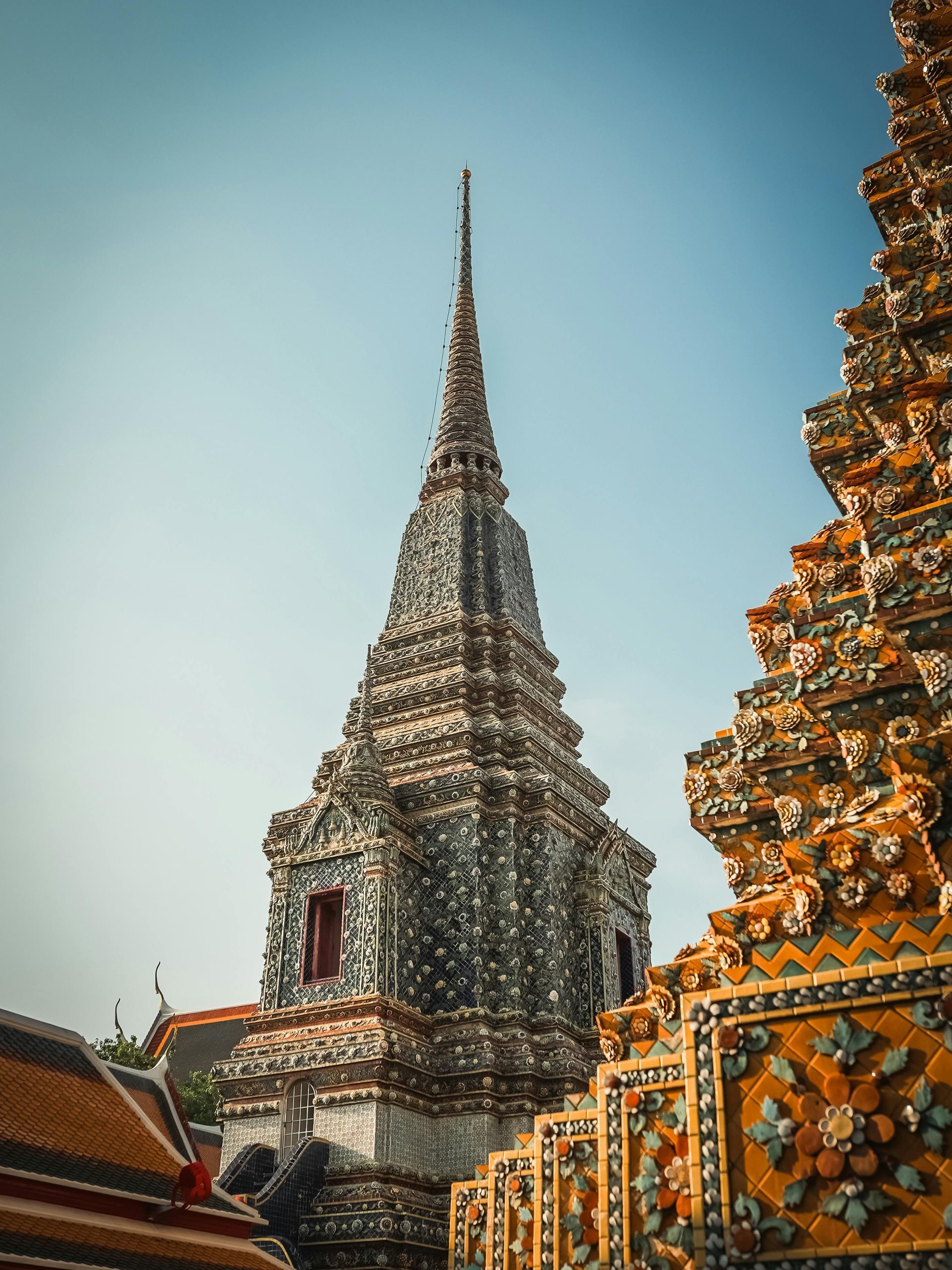 Intricate, ornate temple spire against a clear blue sky in Thailand. Detailed mosaic-like decorations.