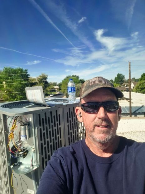 Man in sunglasses and cap beside rooftop HVAC unit under a blue sky