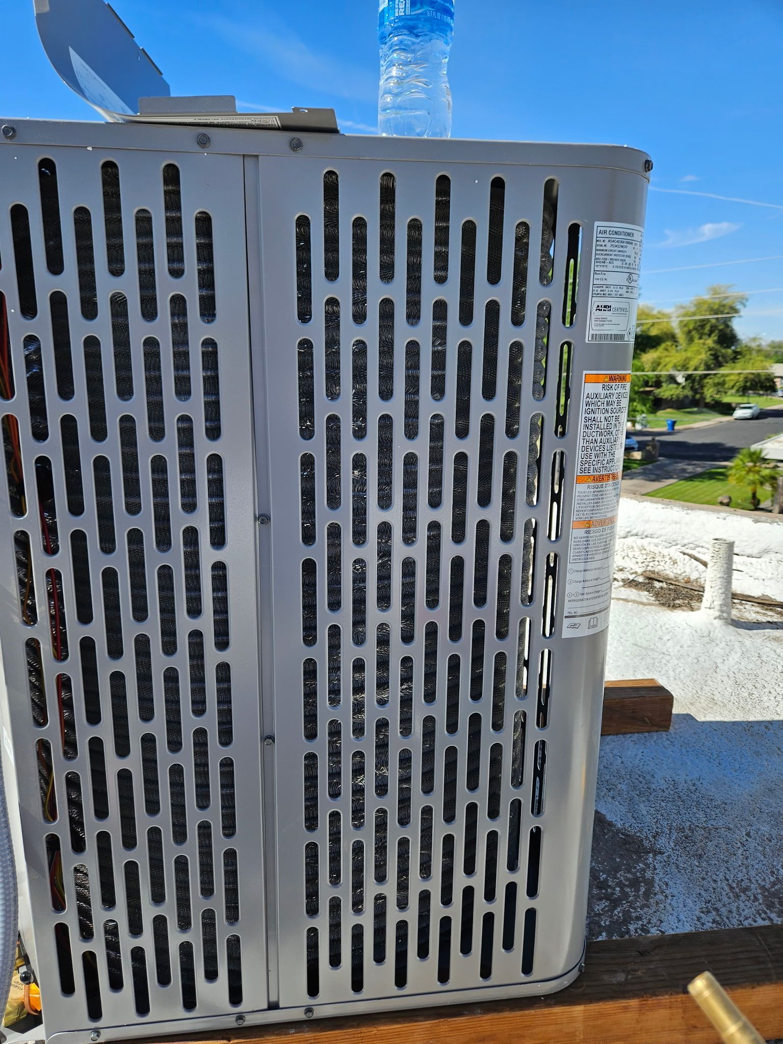 Outdoor HVAC unit with white vented metal panels beside a building under a clear blue sky