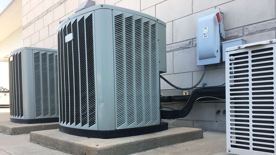 Outdoor HVAC units beside a building wall, with a gray electrical box and conduit attached