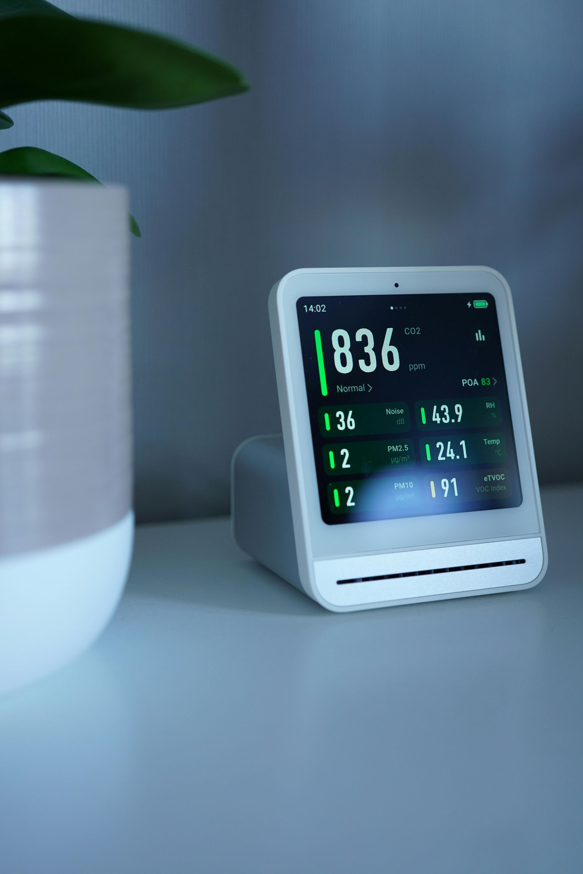 Digital desk clock on a white table beside a plant in soft natural light