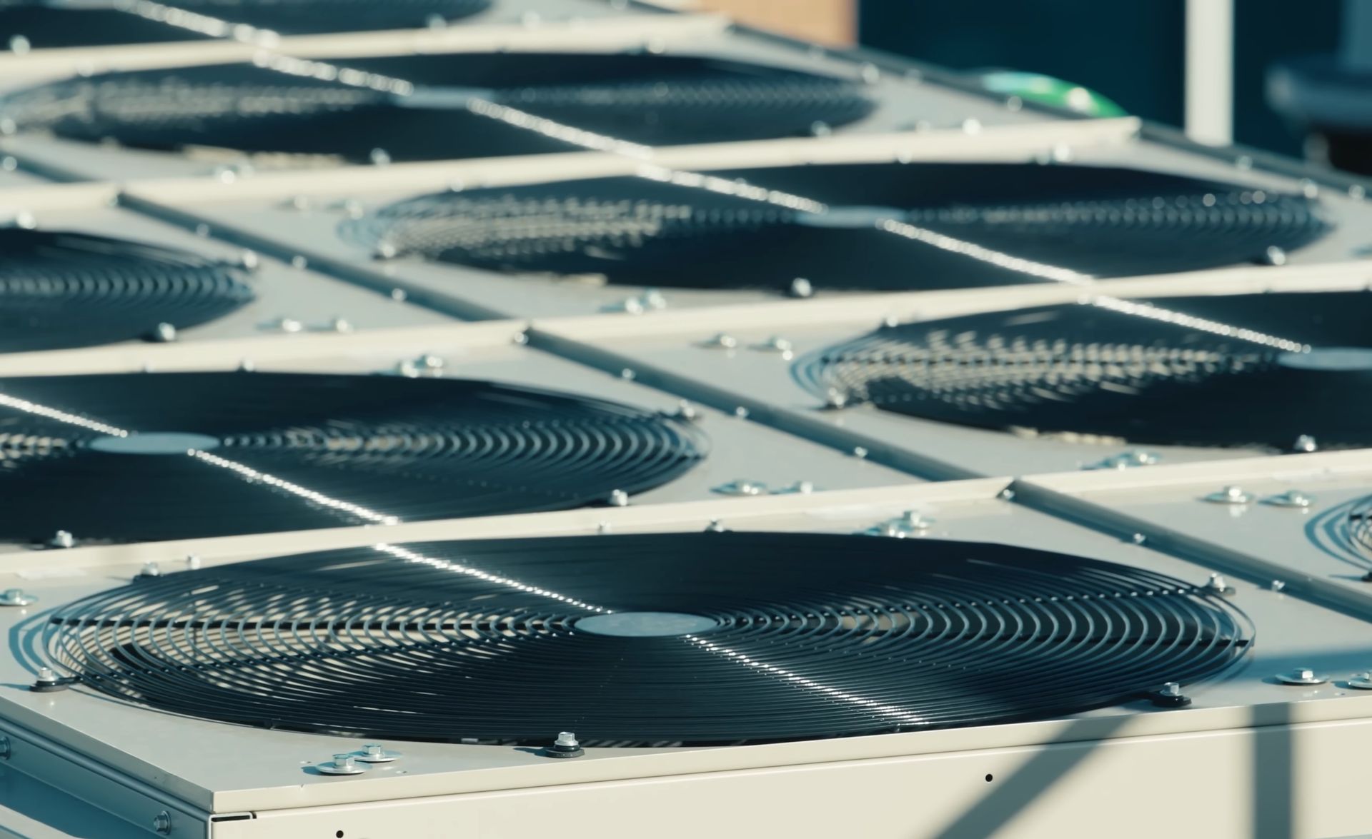 Row of outdoor HVAC condenser units with black fans on a rooftop or industrial platform.