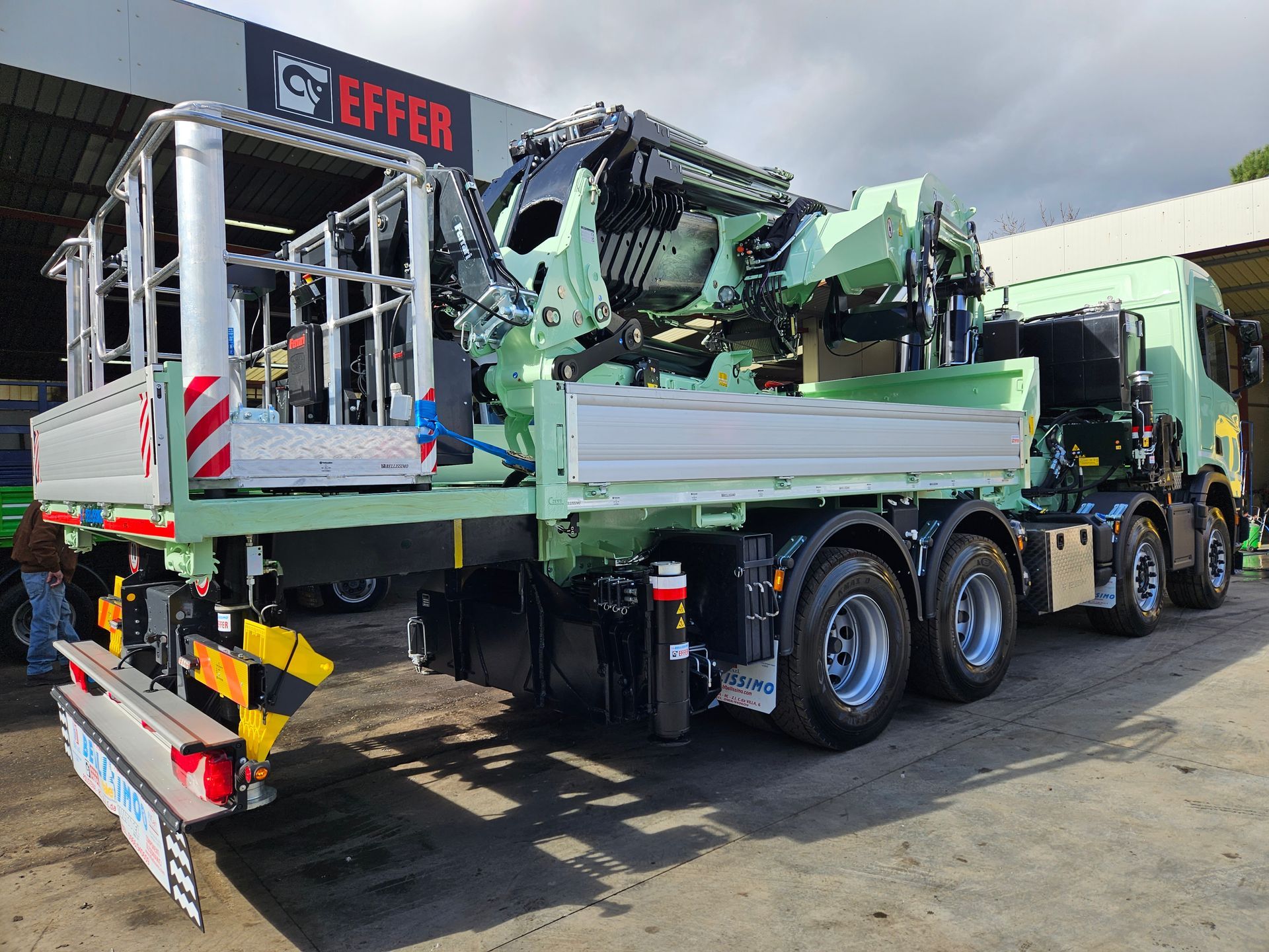 A green truck with a crane on the back is parked in front of a building.
