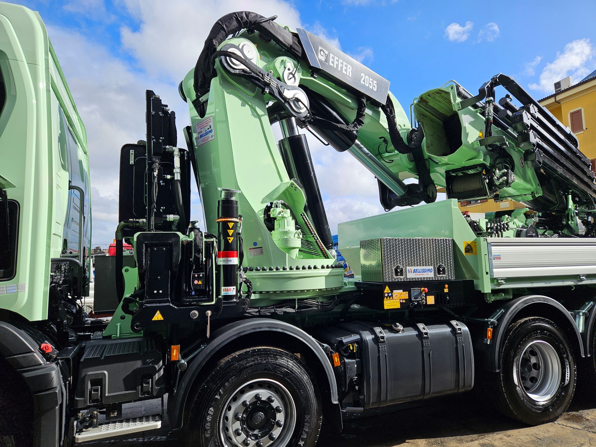 A green truck with a large crane on the back is parked in a parking lot.