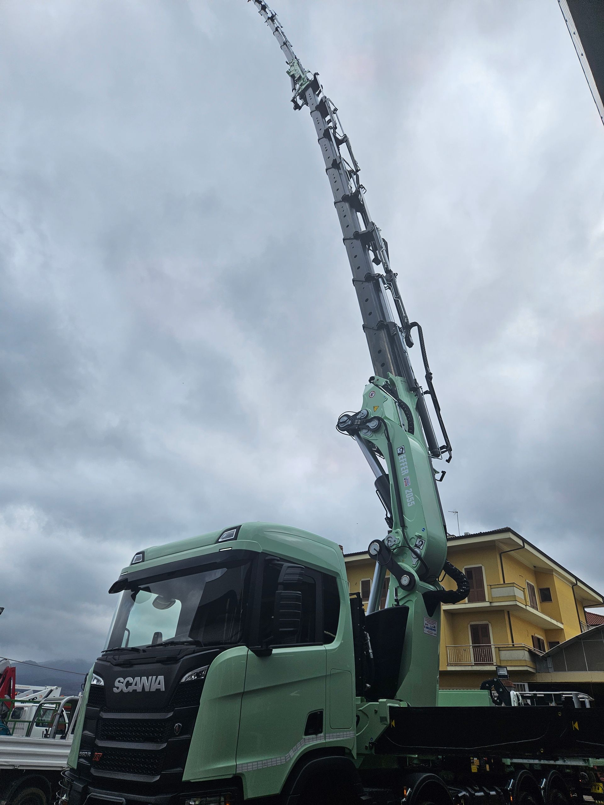 A green truck with a crane attached to it is parked in front of a building.