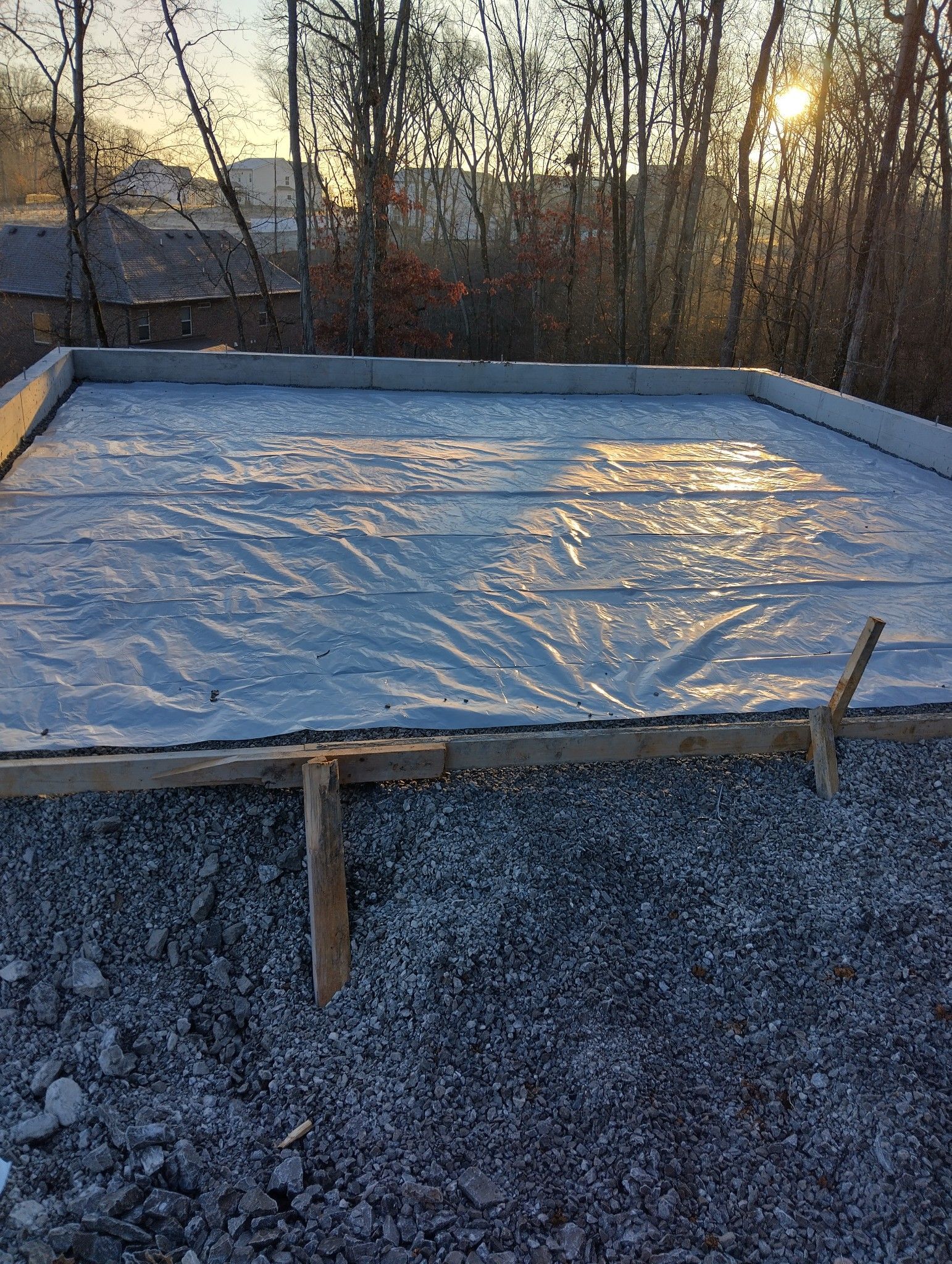 Concrete slab base with a tarp, within a wooden frame, on gravel