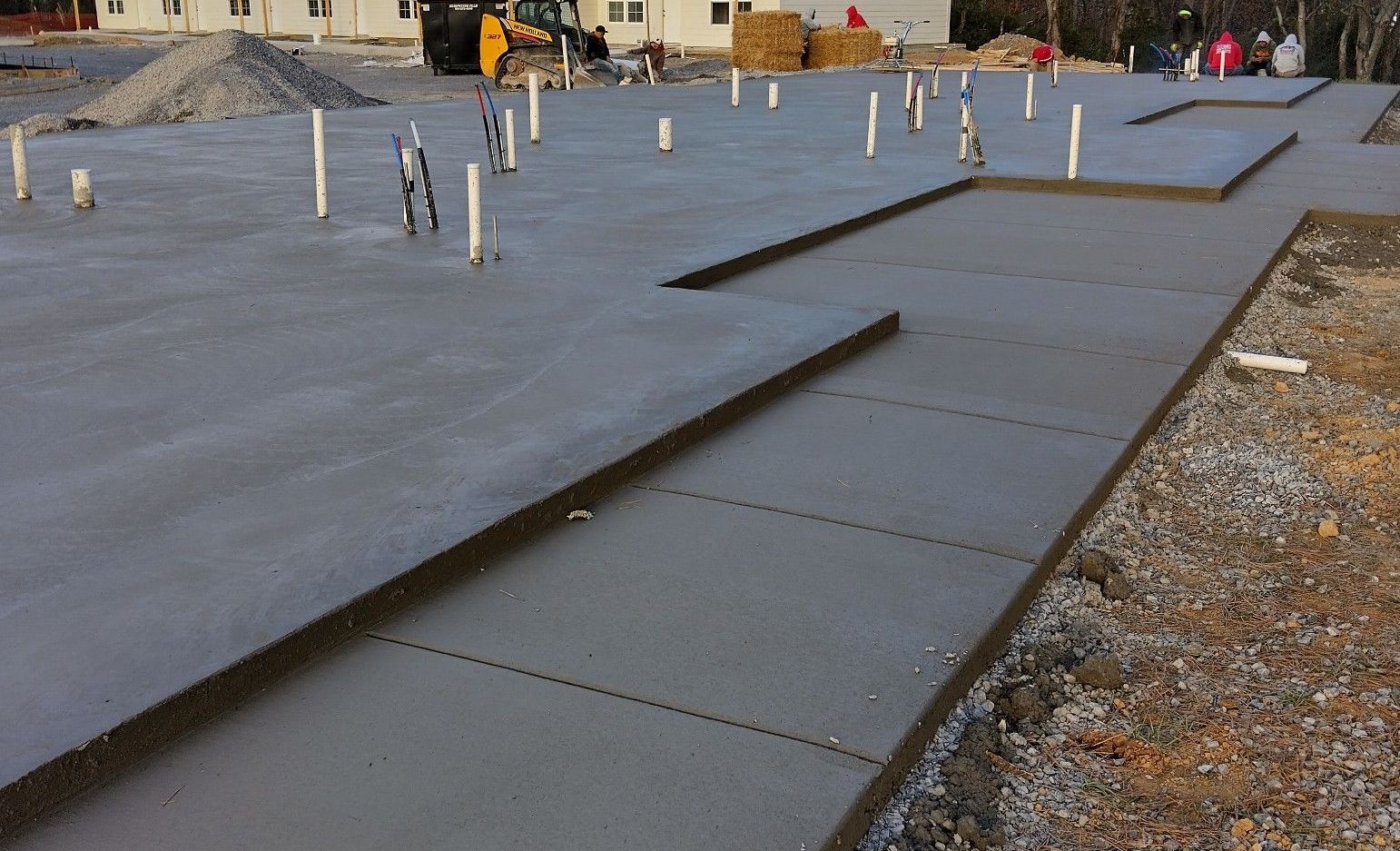 Flat gray roof under construction with black membrane strips and workers in the background