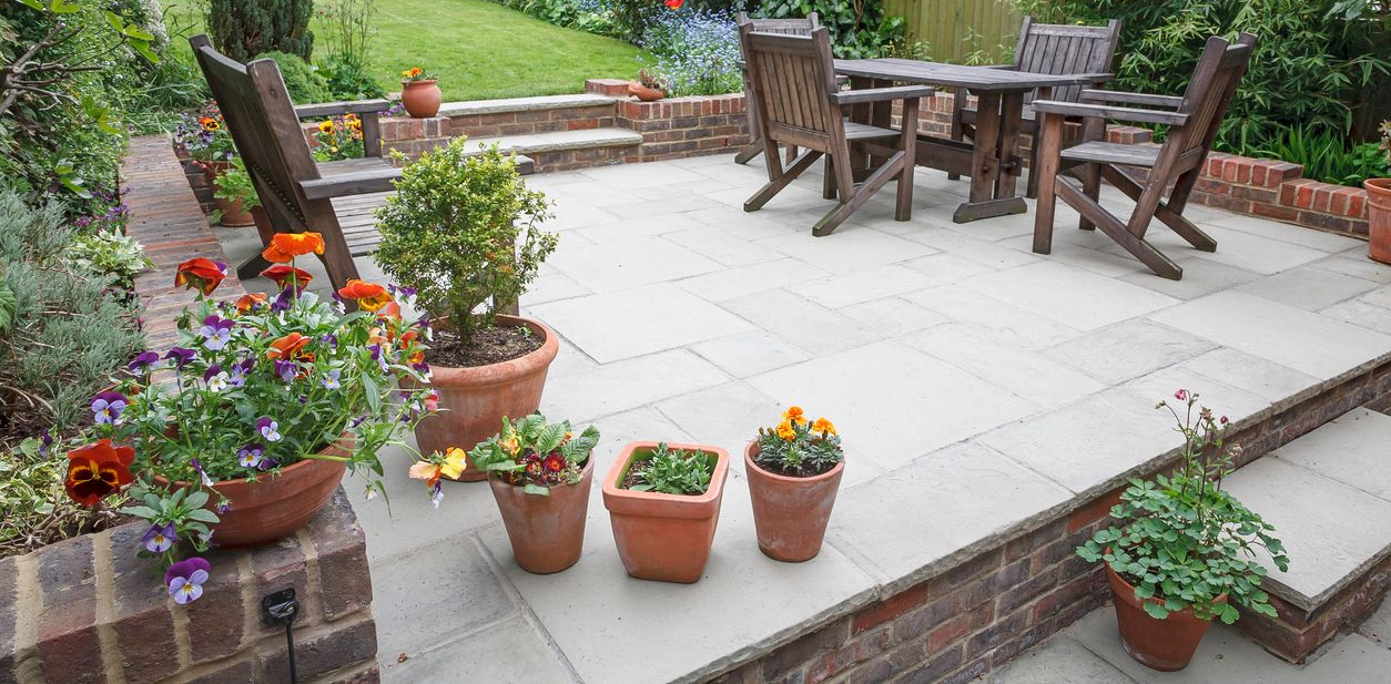 Potted flowers on a brick patio with a small table and chairs in a garden setting