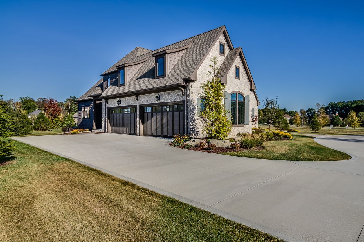 Stone house with large windows and a driveway, set on a sunny grassy lot.