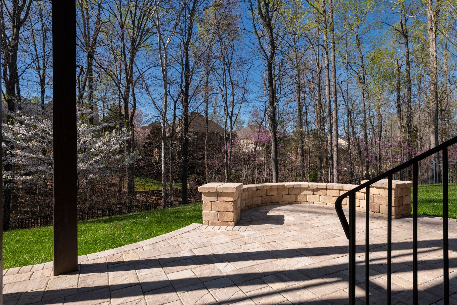 Stone bench in a sunny park with bare trees, grass, and black metal railings.