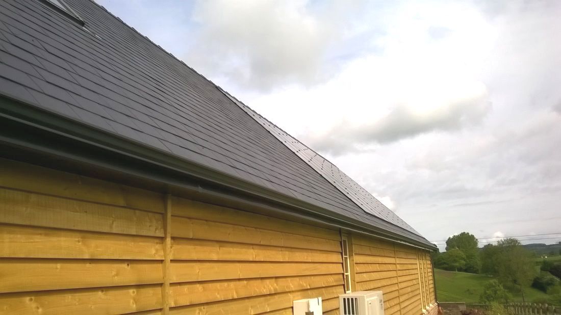 Heavy rain pouring off a brown slate roof into a seamless aluminium gutter system