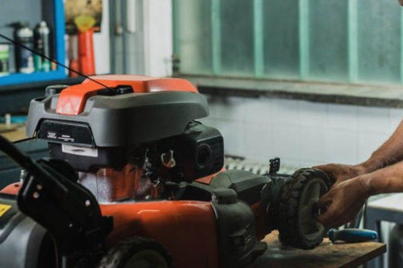 Una persona utilizza una smerigliatrice su un banco da lavoro accanto a una macchina arancione e nera in un'officina.