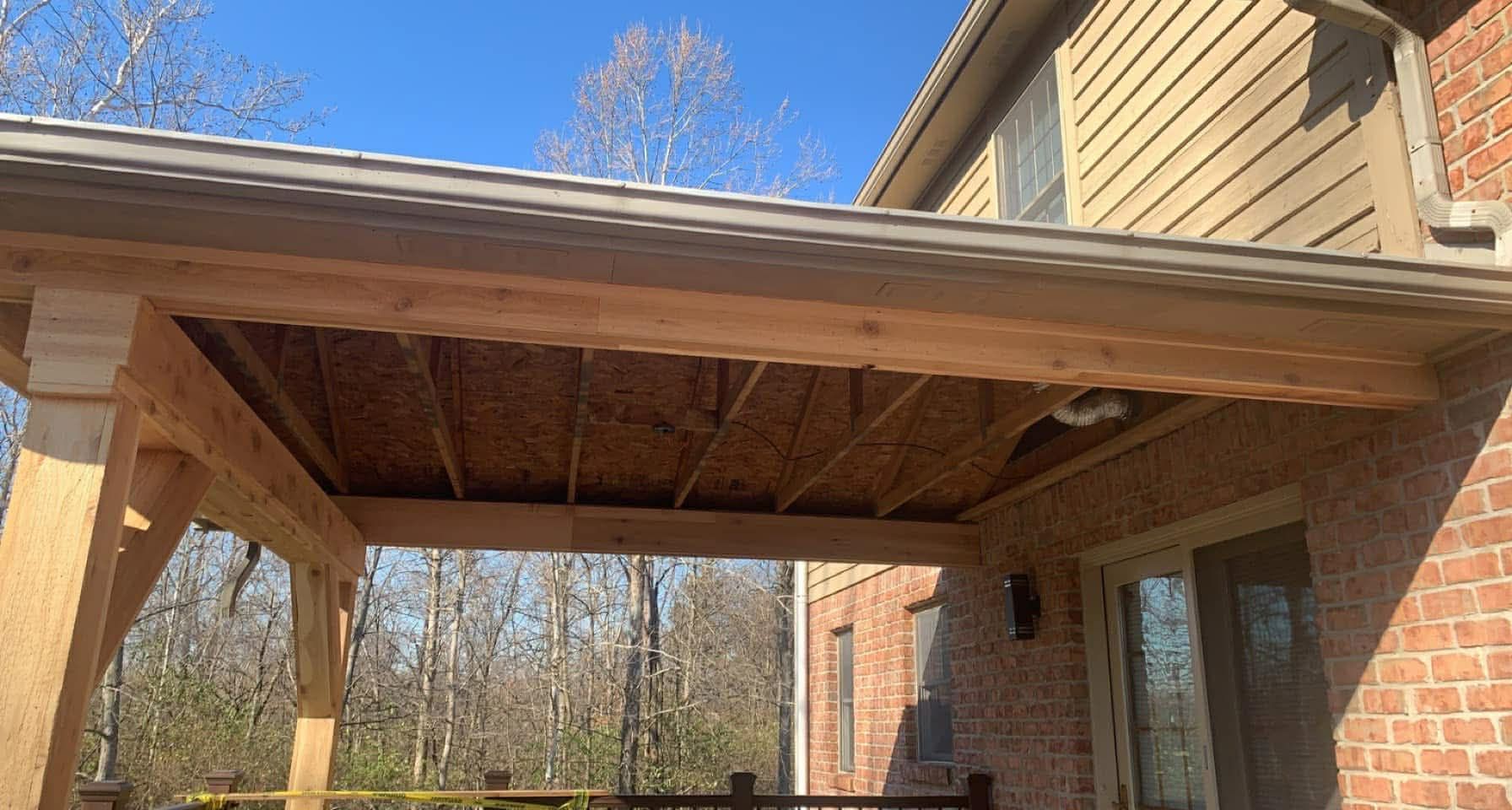 Wooden pergola attached to a brick and siding house, against a clear blue sky.