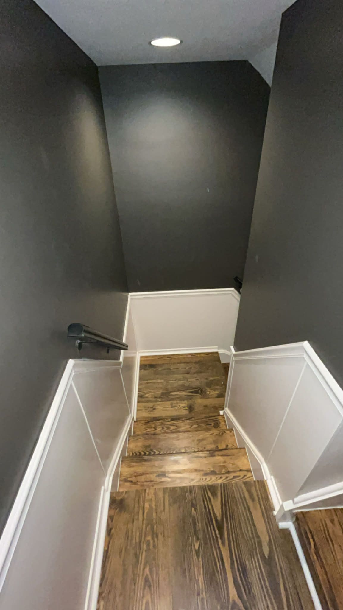 Staircase with dark gray walls and wood-look flooring. White trim accents the stairs and a black handrail.