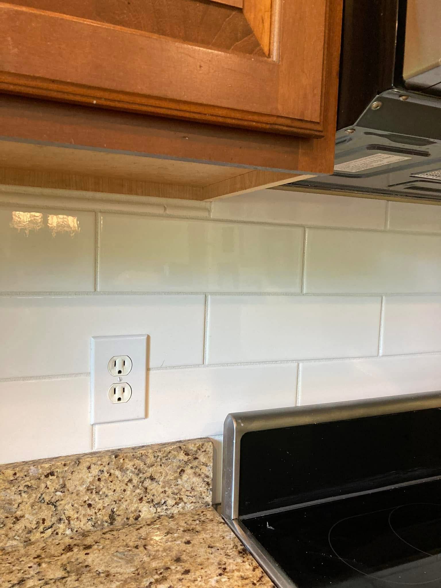 White subway tile backsplash with an electrical outlet and a granite countertop.