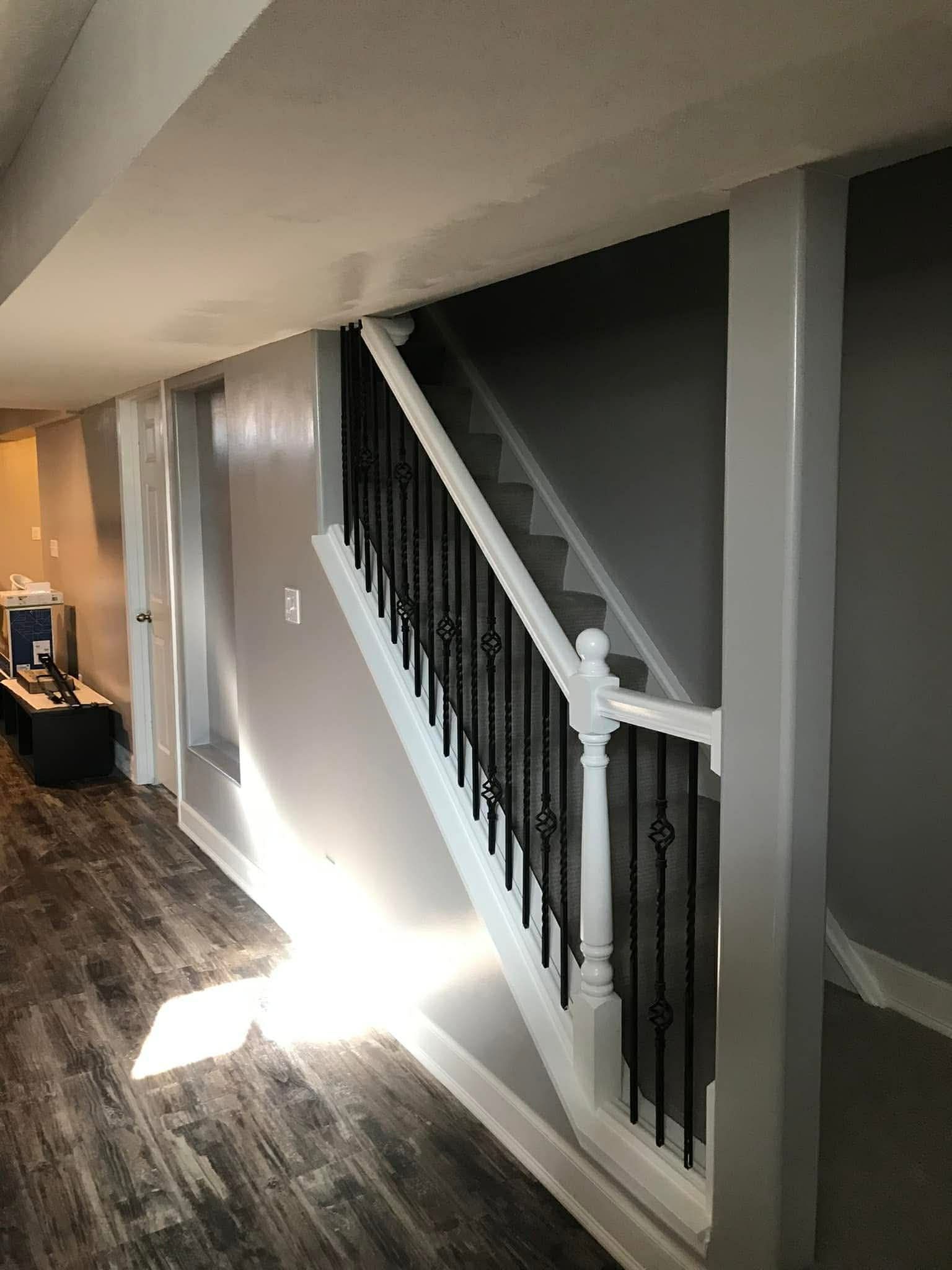 Staircase with white balustrade and black spindles in a room with wood-look flooring and gray walls.