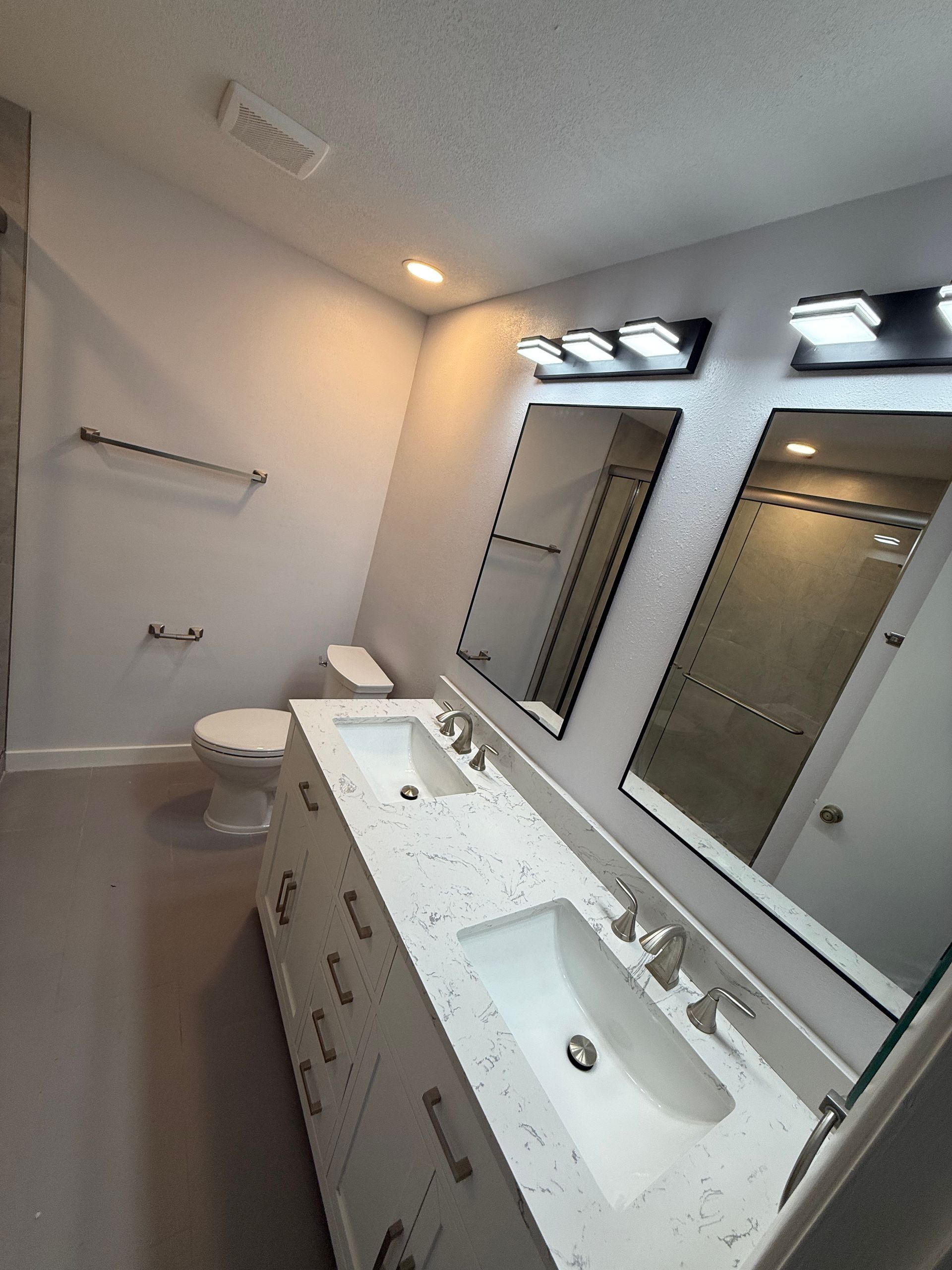 A modern bathroom with a double white vanity, speckled countertops, two mirrors with black lights, and a toilet.