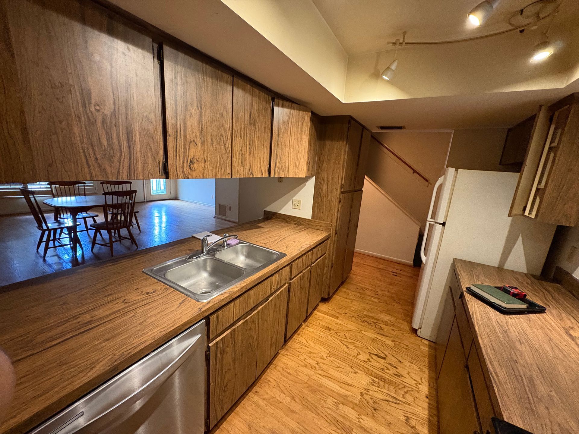A kitchen with wood-toned cabinets and countertops, a stainless steel dishwasher and sink, and a white refrigerator.